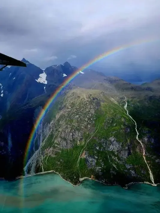 A rainbow is seen from the air as it passes over mountains.