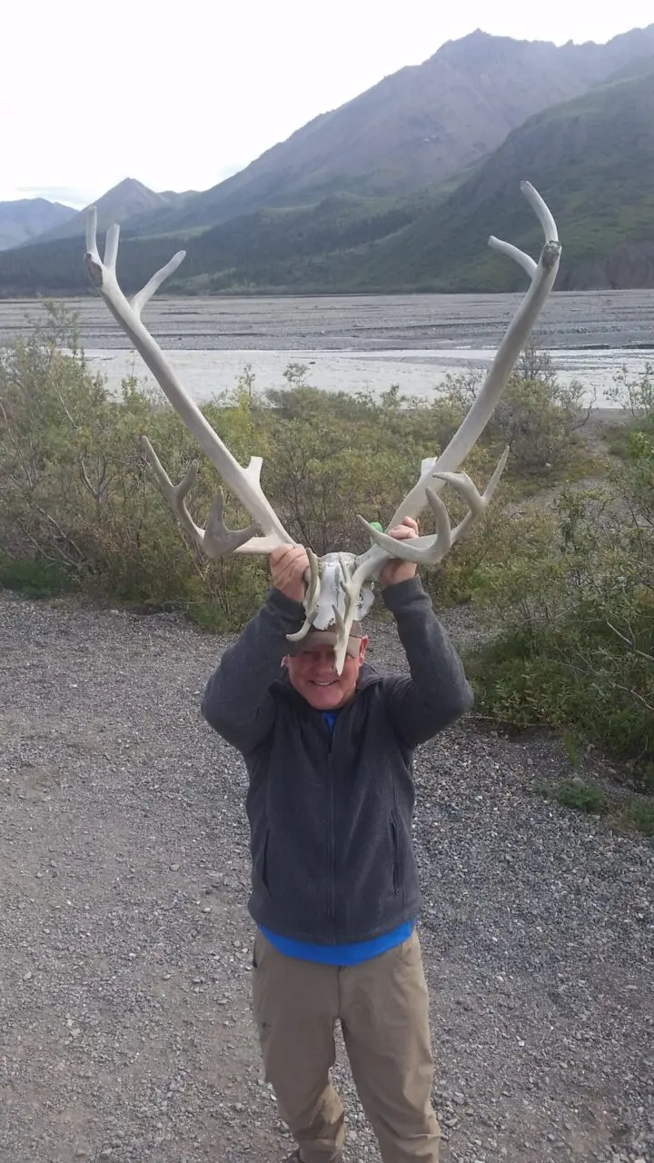 A man holding up two large antlers on his head.