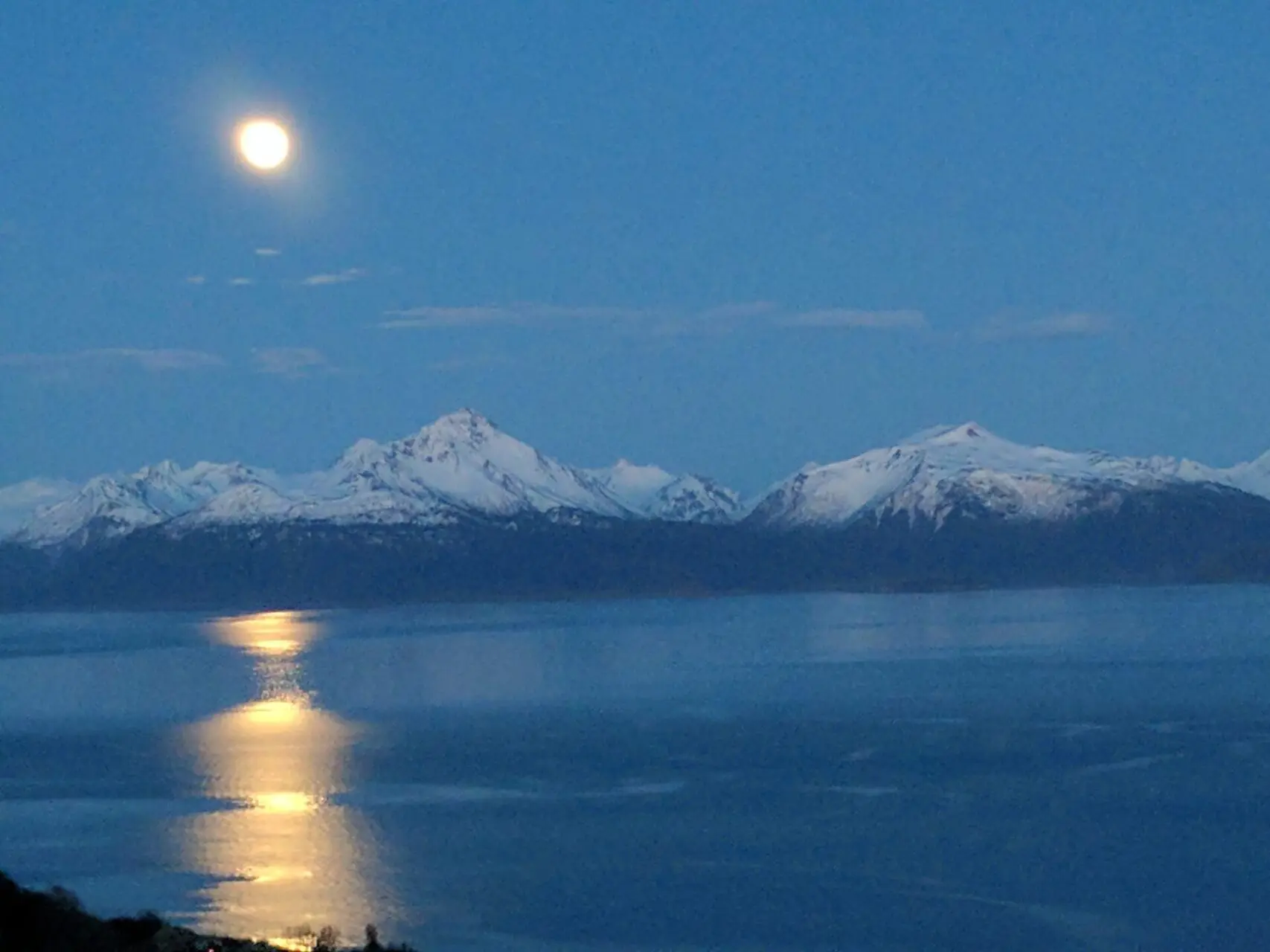 A full moon over the mountains and water.